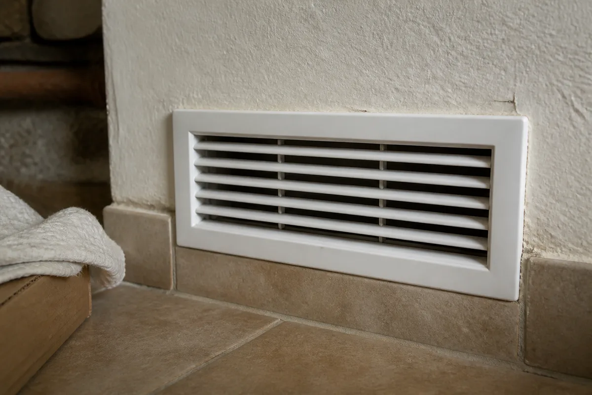 Grille d&rsquo;aération basse dégagée dans un mur de chaufferie avant contrôle
